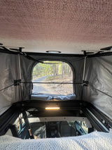 Comfortable RV rental interior with pop-top tent open to a scenic wooded road. Perfect for camping adventures.