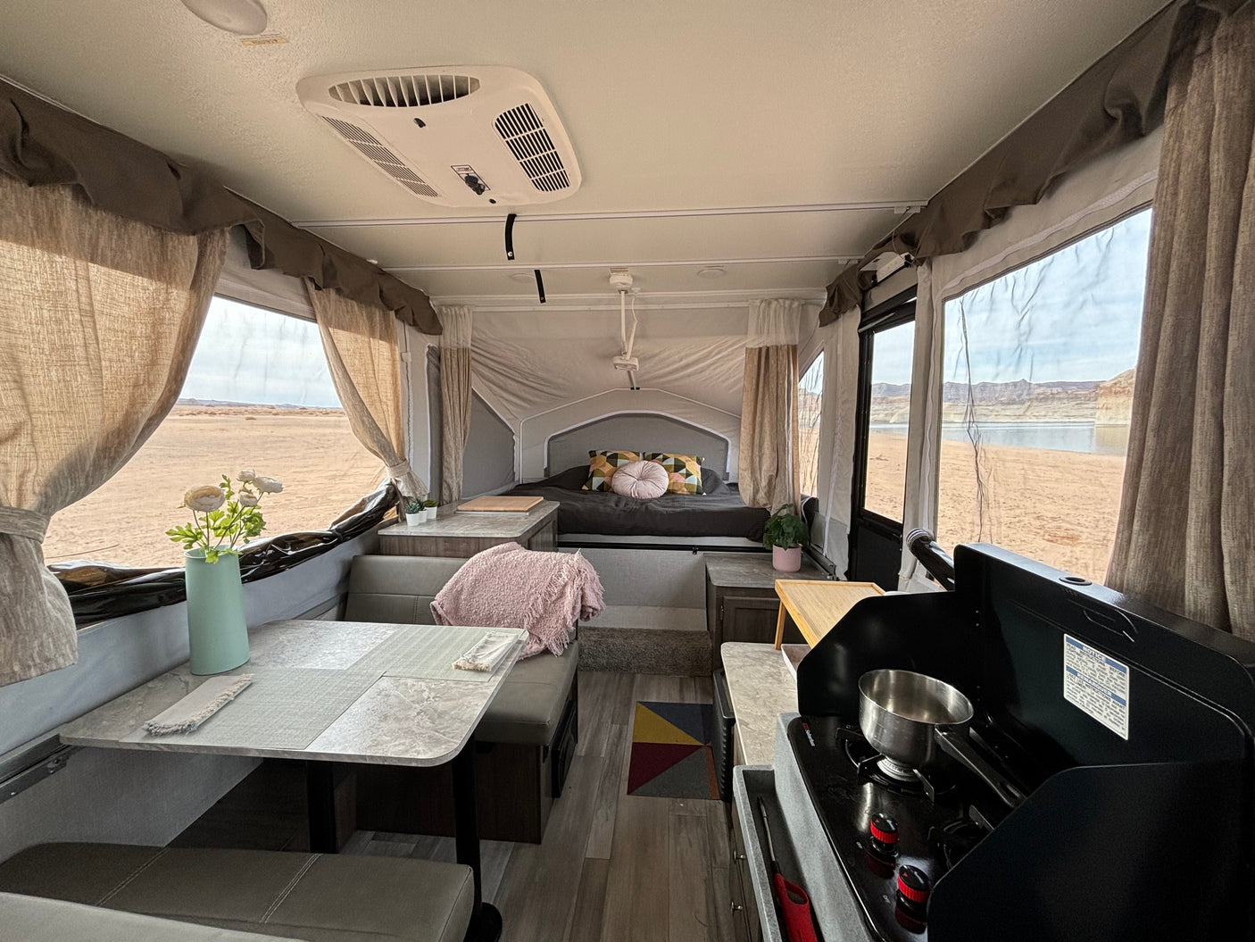 Inside a cozy rv rental, showing the dining area, bed, and kitchen with stunning desert and lake views.