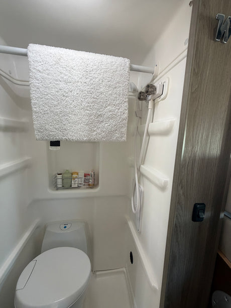 Compact RV rental bathroom featuring a shower, toilet, and toiletries. A white towel hangs on a rod above the toilet.