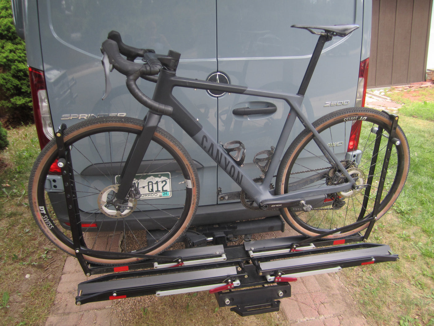 A sleek Canyon gravel bike is securely mounted on a hitch rack attached to a grey Sprinter van, perfect for an RV rental adventure.