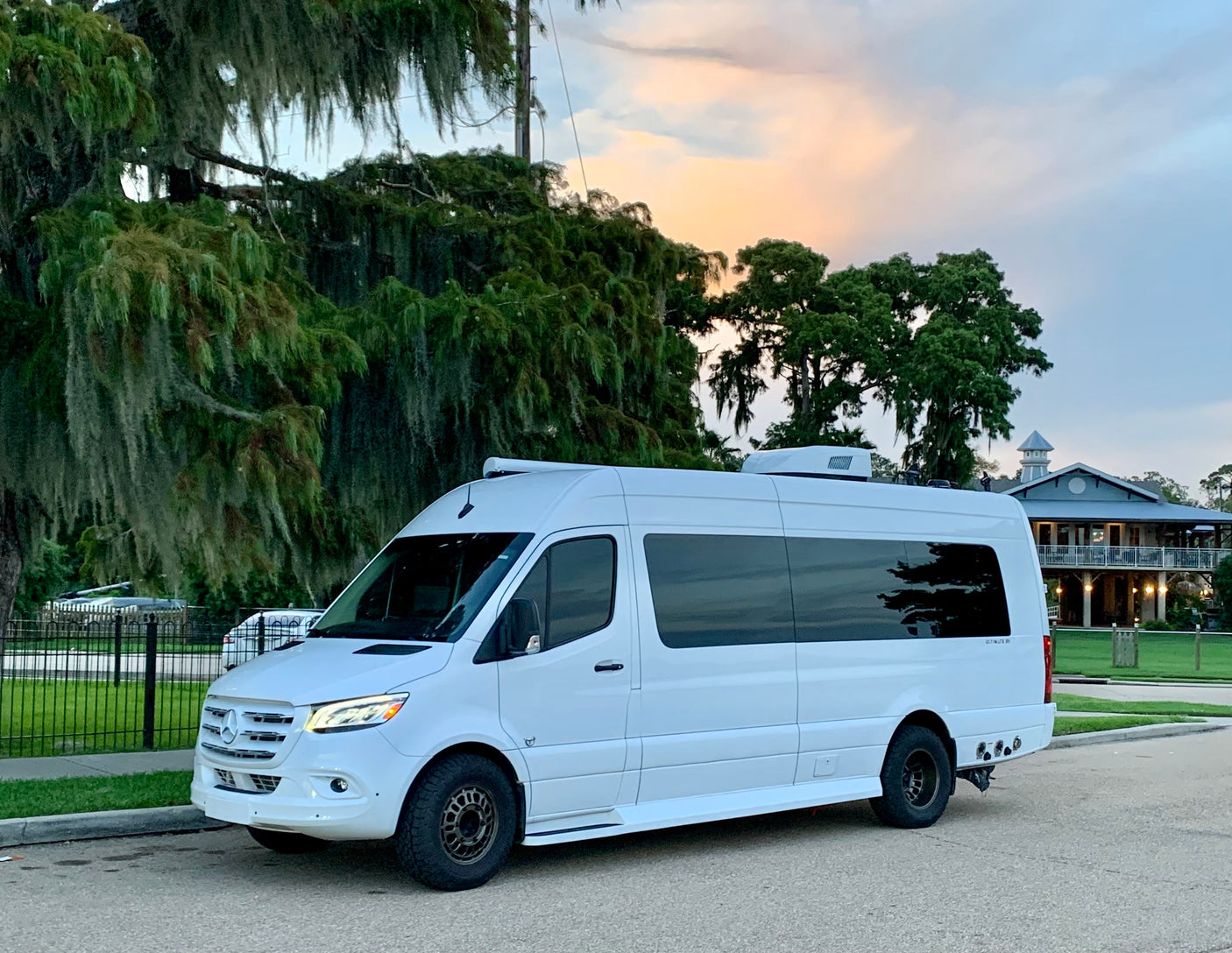 White Mercedes Sprinter camper van, ideal for your next rv rental adventure, parked on a street with Spanish moss trees and a sunset sky.