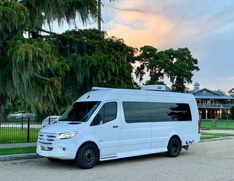 White Mercedes Sprinter camper van, ideal for your next rv rental adventure, parked on a street with Spanish moss trees and a sunset sky.
