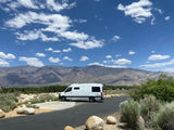 White rv rental parked with majestic mountains under a blue sky. Ideal for a scenic outdoor getaway.