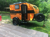 Orange Sunray teardrop camper, an ideal RV rental. Parked on grass at a sunny campsite, ready for adventure!