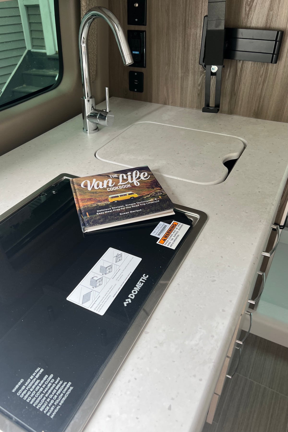 RV rental compact kitchen with sink, Dometic cooktop, and "The Van Life Cookbook" on the counter. — photo 19