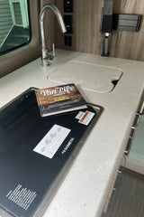 RV rental compact kitchen with sink, Dometic cooktop, and "The Van Life Cookbook" on the counter.