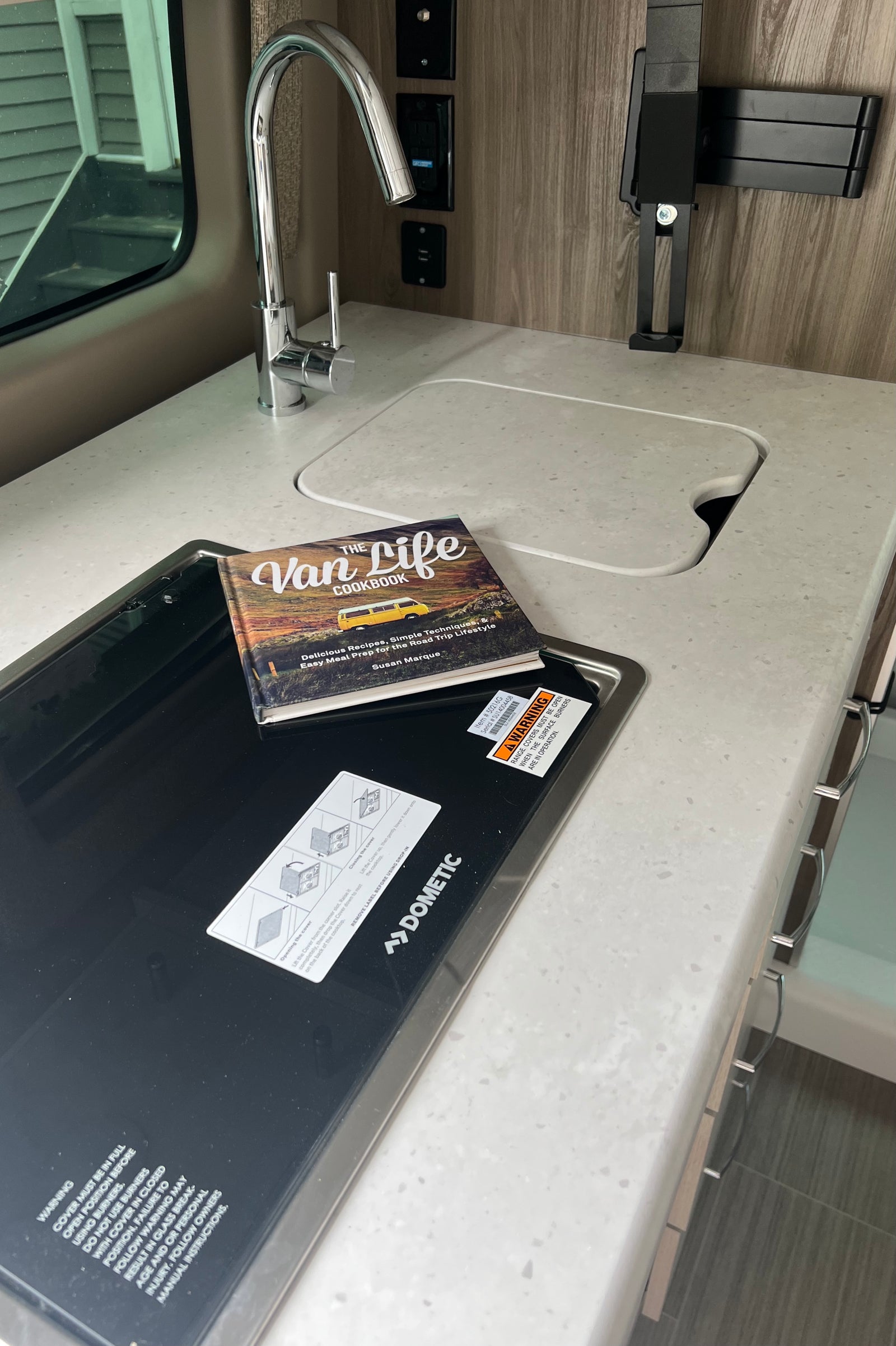 RV rental compact kitchen with sink, Dometic cooktop, and "The Van Life Cookbook" on the counter.