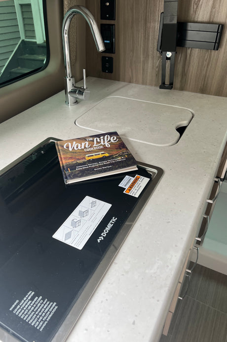 RV rental compact kitchen with sink, Dometic cooktop, and "The Van Life Cookbook" on the counter.