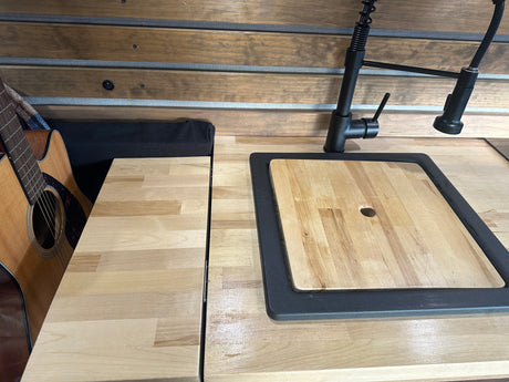 RV rental interior: wood kitchen counter with sink/cutting board, black faucet, and an acoustic guitar.