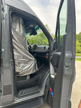 Open driver door of a grey RV rental van with a silver thermal privacy curtain across the windshield.