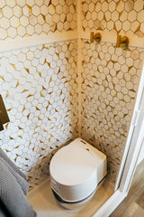 Modern RV rental wet bath features stylish gold & white hexagon tiles and a compact toilet.