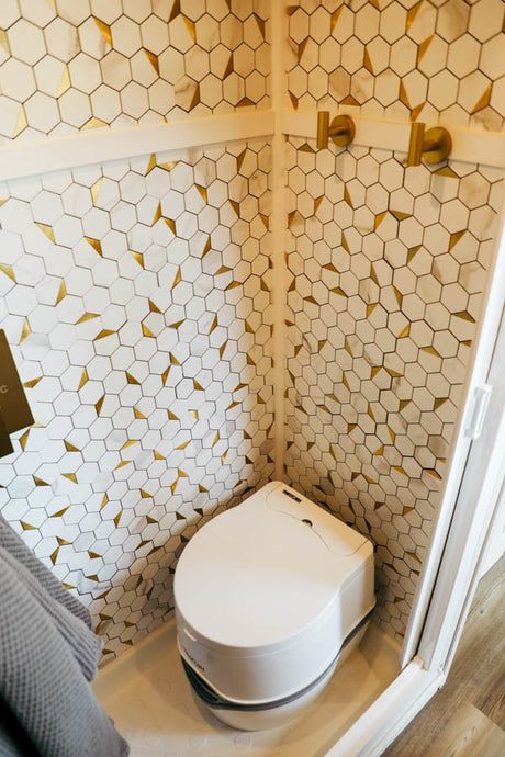 Modern RV rental wet bath features stylish gold & white hexagon tiles and a compact toilet.