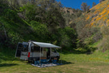 RV rental camper van parked in a scenic valley with green hillsides & orange wildflowers under a clear blue sky.