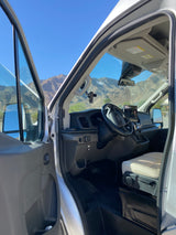 RV rental van interior: open door reveals driver's seat, dashboard, and scenic mountain views on a sunny day.
