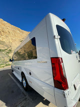 White Coachmen RV rental parked by sunny mountains under a blue sky with a crescent moon. Perfect for a road trip!