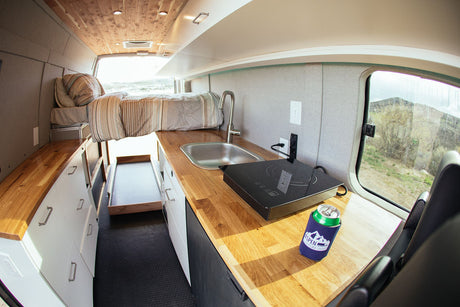 Inside a modern RV rental, this custom van conversion offers a bed, functional kitchen with sink & cooktop, plus storage.