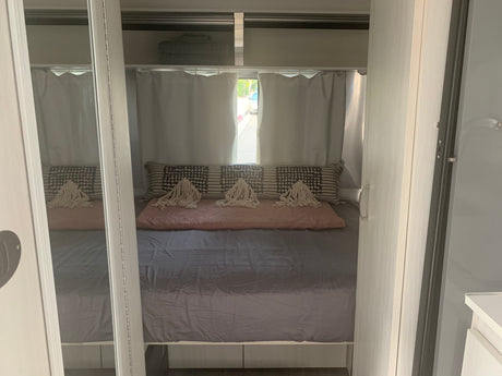 Inside an RV rental: a compact bedroom with a bed, decorative pillows, window curtains, and mirrored storage.
