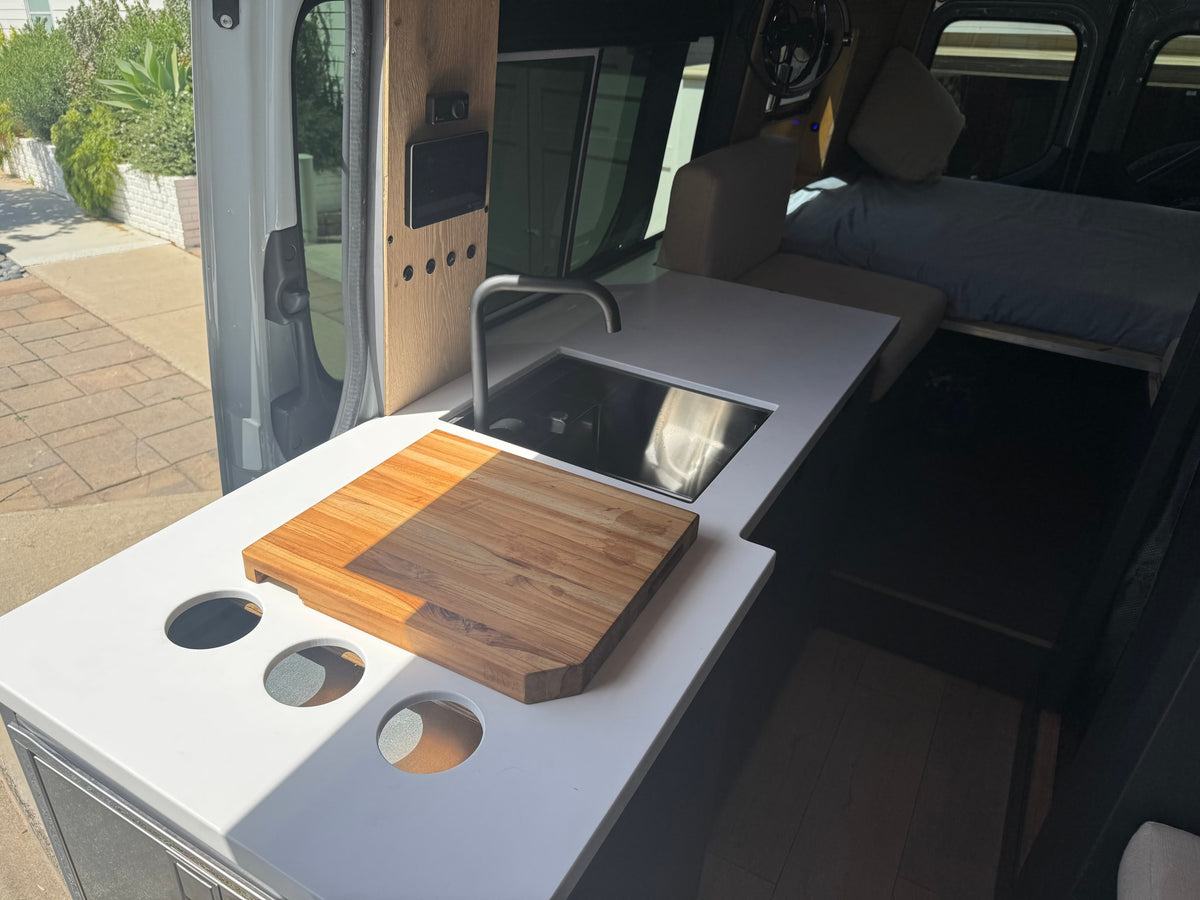 RV rental: Camper van interior with a modern kitchenette, sink, cutting board, control panel, and a cozy bed. — photo 10