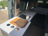 RV rental: Camper van interior with a modern kitchenette, sink, cutting board, control panel, and a cozy bed.