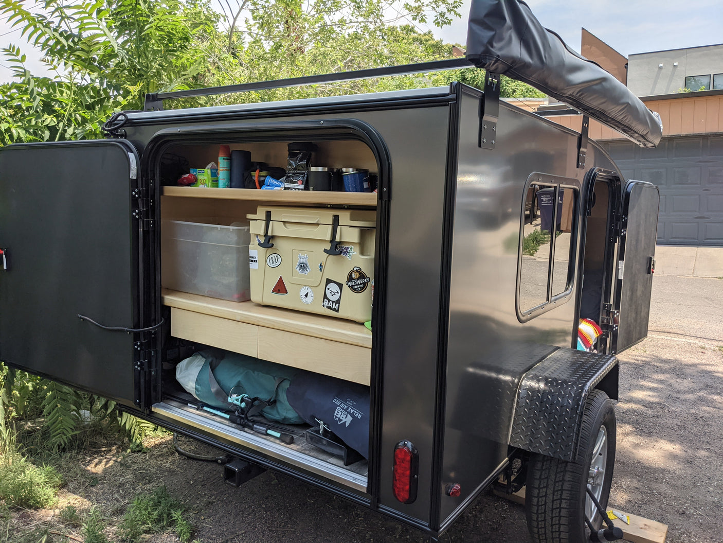 This RV rental teardrop trailer shows its open rear galley with camping gear, cooler, and fishing rods. An adventure-ready setup.