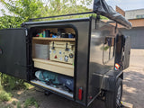 This RV rental teardrop trailer shows its open rear galley with camping gear, cooler, and fishing rods. An adventure-ready setup.