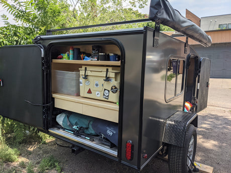 This RV rental teardrop trailer shows its open rear galley with camping gear, cooler, and fishing rods. An adventure-ready setup.