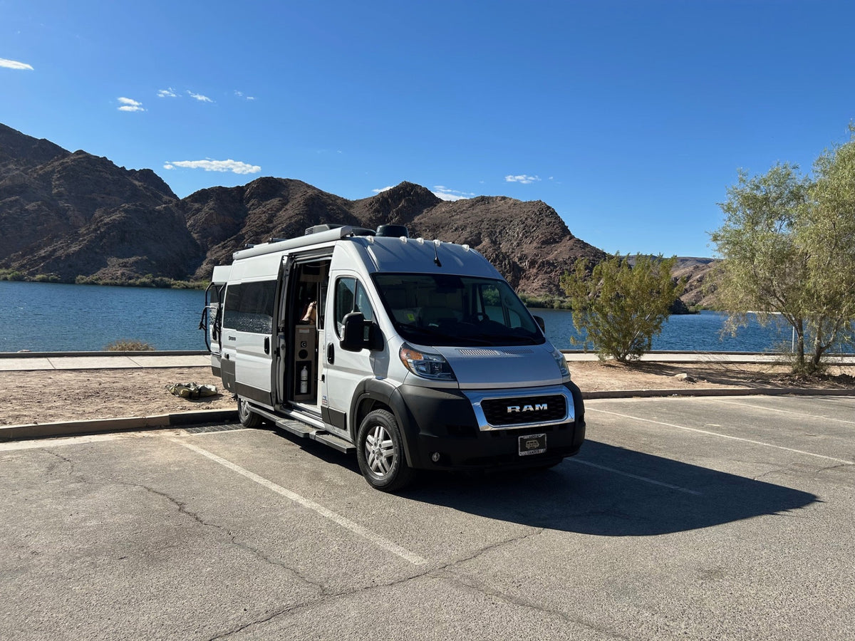  under a clear blue sky. Ideal for outdoor adventures.|Enjoy your RV rental: a white camper van parked lakeside with majestic mountains under a blue sky.|White RV rental parked by a stunning lake and mountains under a clear sky. Side door open — photo 10