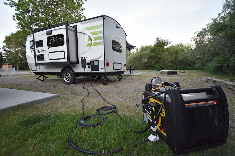 RV rental travel trailer parked at a rustic campsite, powered by a large portable generator on the grass.