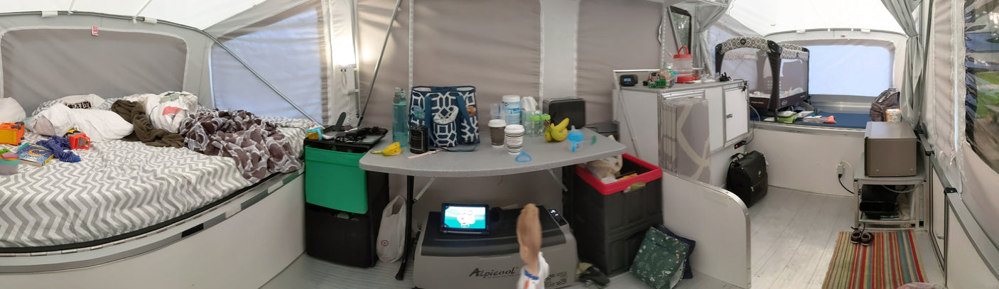 Lived-in RV rental camper interior featuring beds, a central table with bottles and bananas, and a baby's pack-n-play.