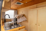 Cozy RV rental interior with ocean view bed, compact kitchen, and wood finishes. Perfect for van life adventures.