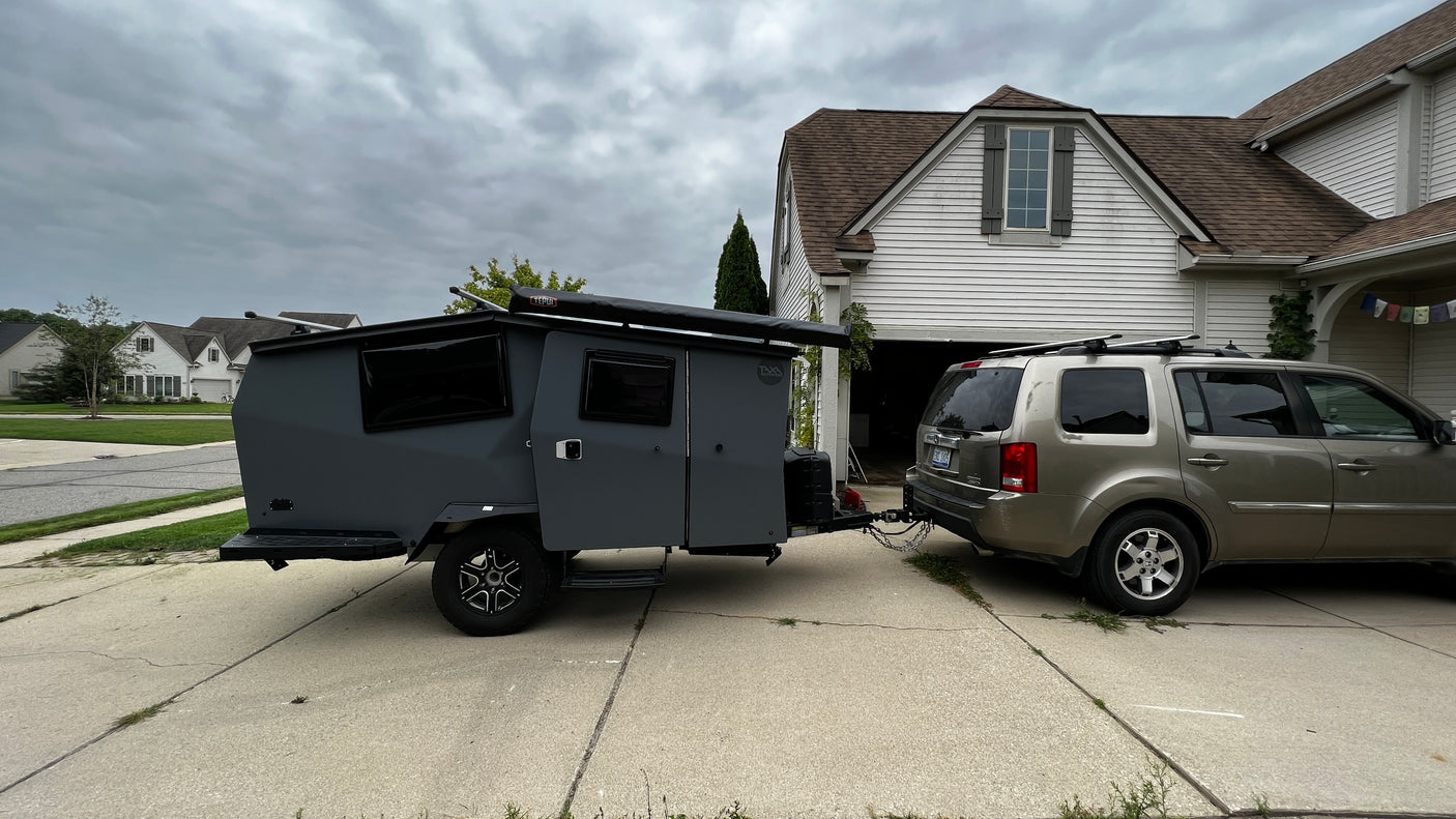 RV rental: A sleek grey camper trailer, hitched to an SUV in a driveway, ready for outdoor adventure.