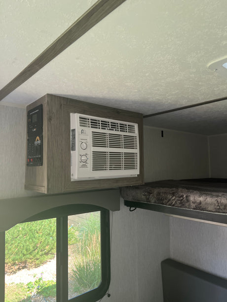 RV rental interior: window AC unit, control panel, window view, and a cozy bunk bed setup.