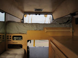 Inside a custom **rv rental** camper van: wooden interior, comfy bed, power hub, and views of palm trees.