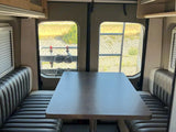 RV rental interior: comfy dinette with upholstered benches, large rear windows showing a fenced outdoor area.