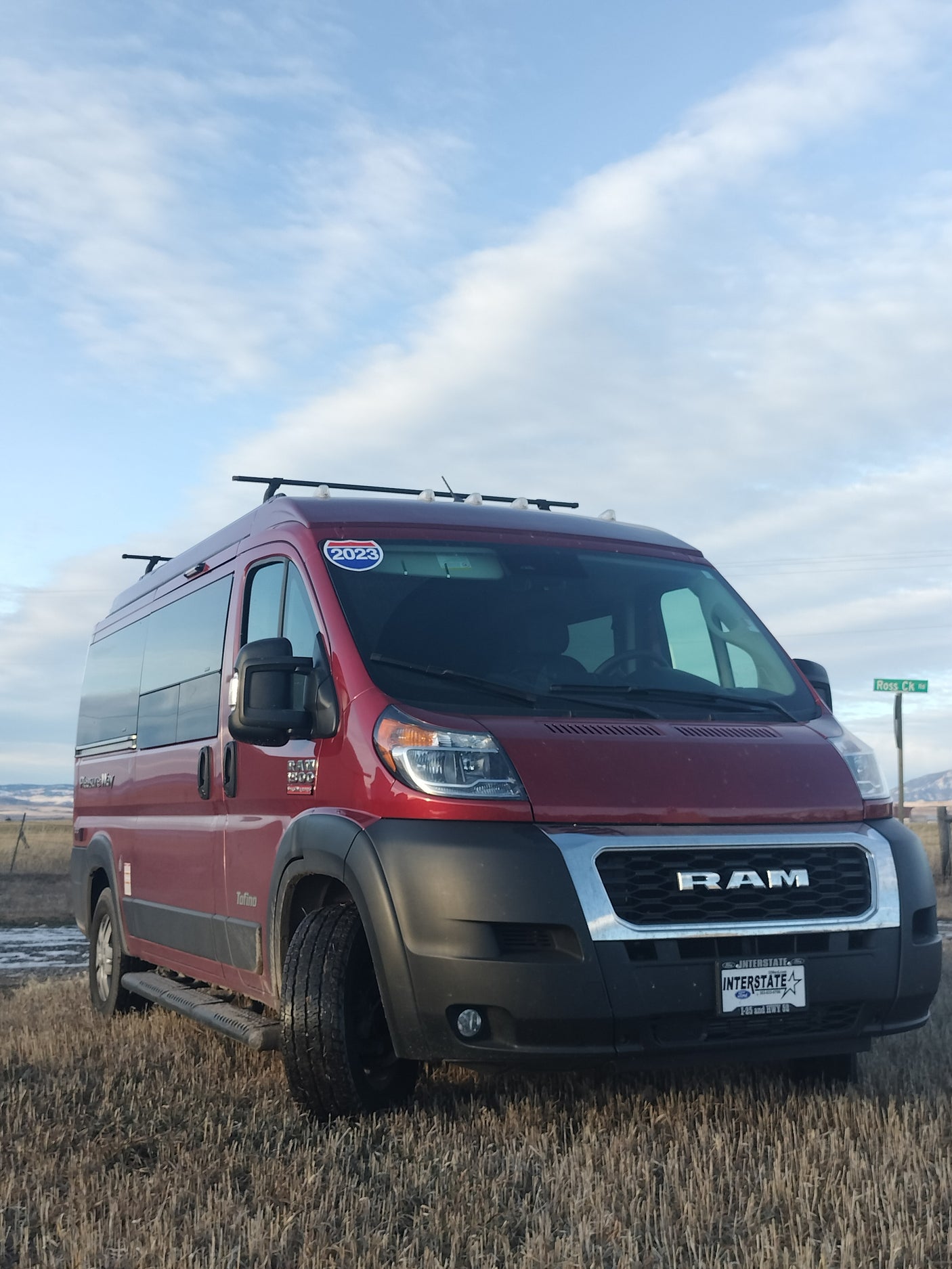 A red Pleasure-Way Tofino camper van, an RV rental, parked in a dry field under a cloudy sky, ready for a road trip.