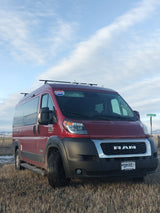 A red Pleasure-Way Tofino camper van, an RV rental, parked in a dry field under a cloudy sky, ready for a road trip.