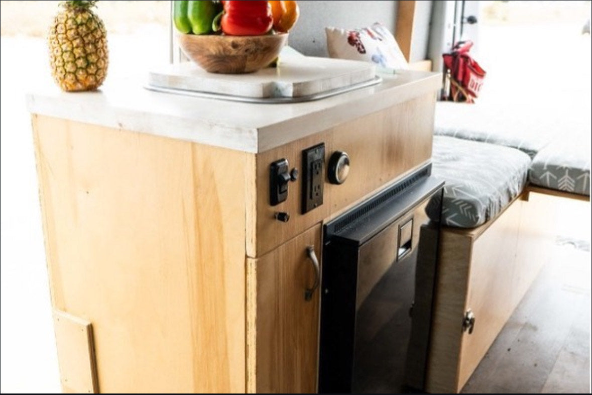 Compact RV rental interior featuring a wooden kitchenette with controls, built-in fridge, and comfortable cushioned seating. — photo 18