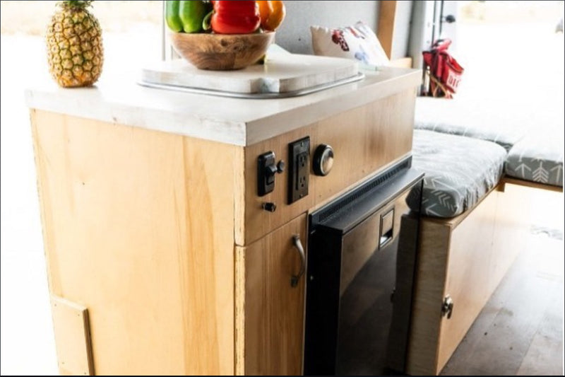 Compact RV rental interior featuring a wooden kitchenette with controls, built-in fridge, and comfortable cushioned seating. — photo 18