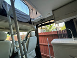 Inside this RV rental, a ladder reaches an upper sleeping area. A kitchen sink is on the right, and driver's seats are visible.