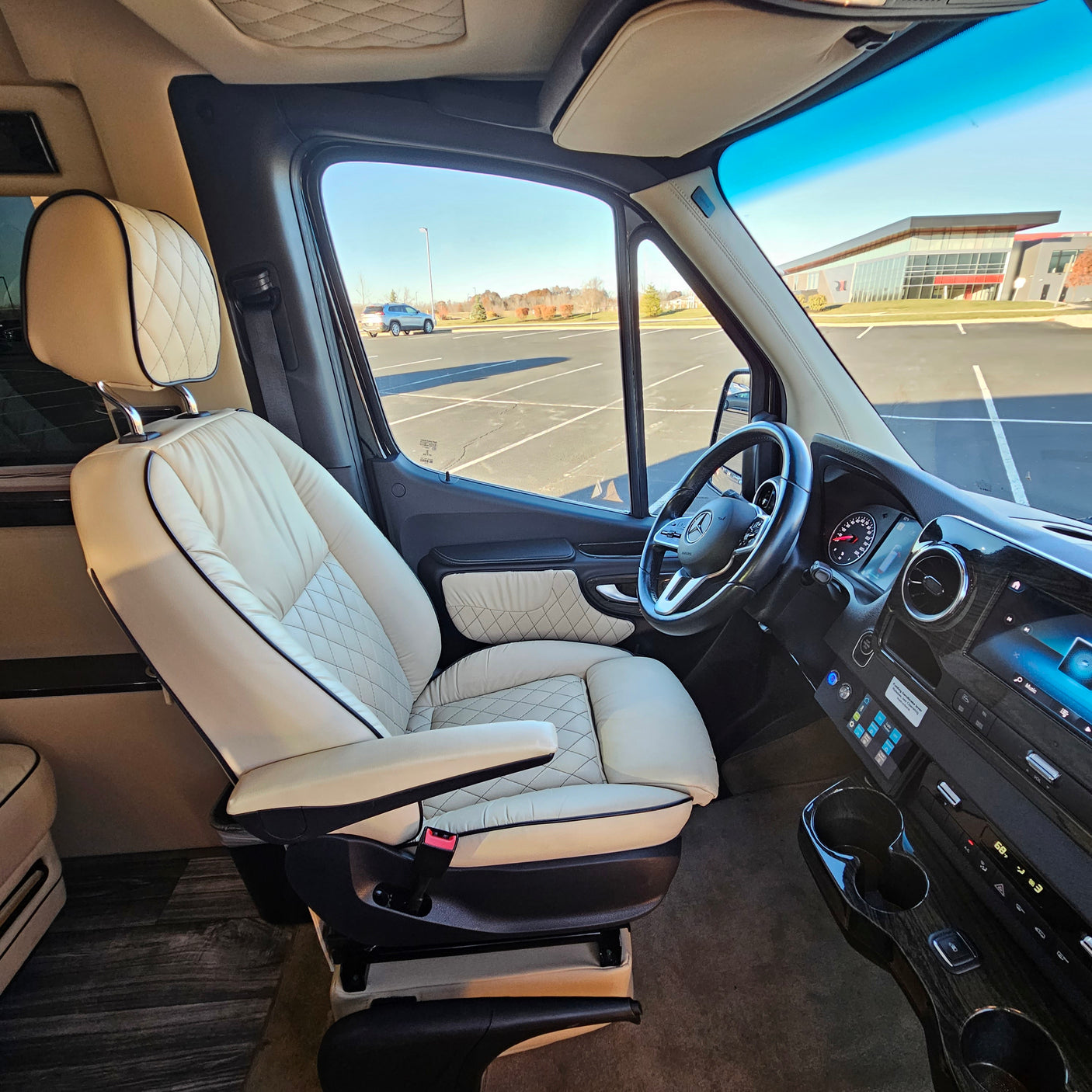Luxurious RV rental interior featuring quilted cream leather swivel seats, wood trim, and a modern dashboard.
