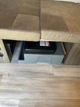 RV rental: Under-bench storage featuring a portable stove, an RV heating/cooling vent, and durable wood-look flooring.