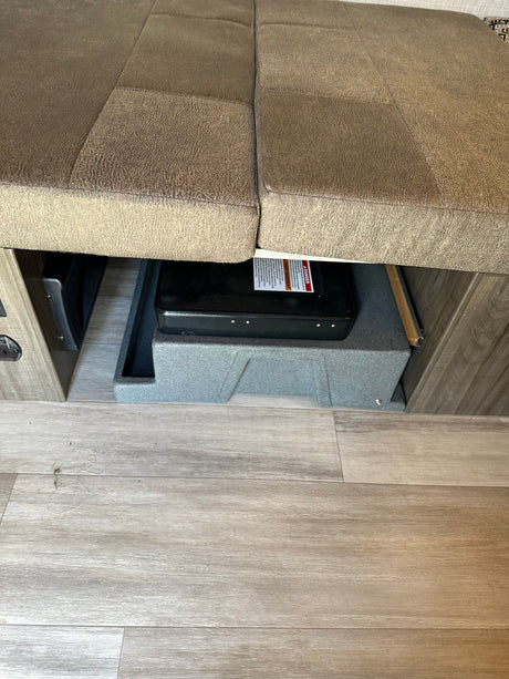 RV rental: Under-bench storage featuring a portable stove, an RV heating/cooling vent, and durable wood-look flooring.