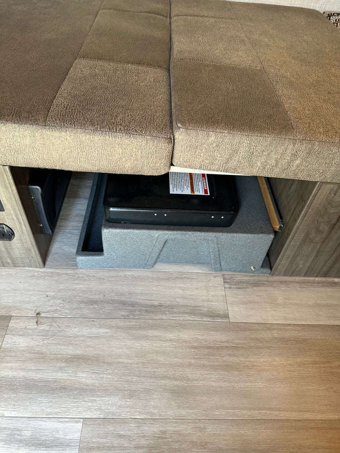 RV rental: Under-bench storage featuring a portable stove, an RV heating/cooling vent, and durable wood-look flooring.