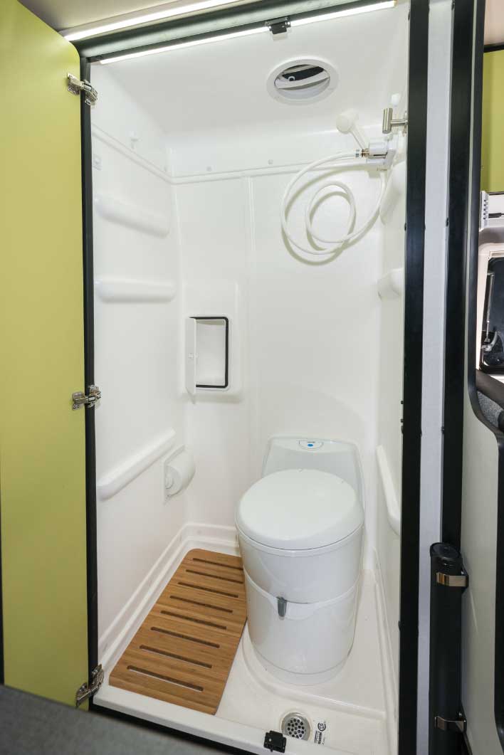 Compact RV rental bathroom features a toilet, shower with hose, and a wooden mat. — photo 10
