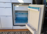 Open rv rental fridge with blue shelves/drawers, integrated into white cabinets, providing essential kitchen storage.