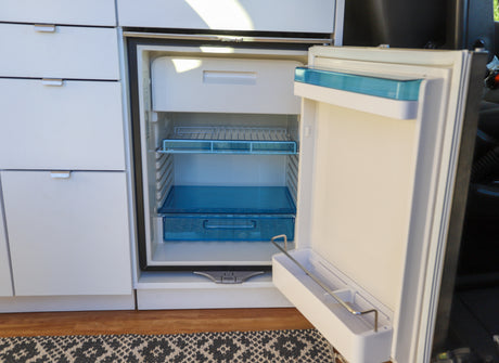 Open rv rental fridge with blue shelves/drawers, integrated into white cabinets, providing essential kitchen storage.