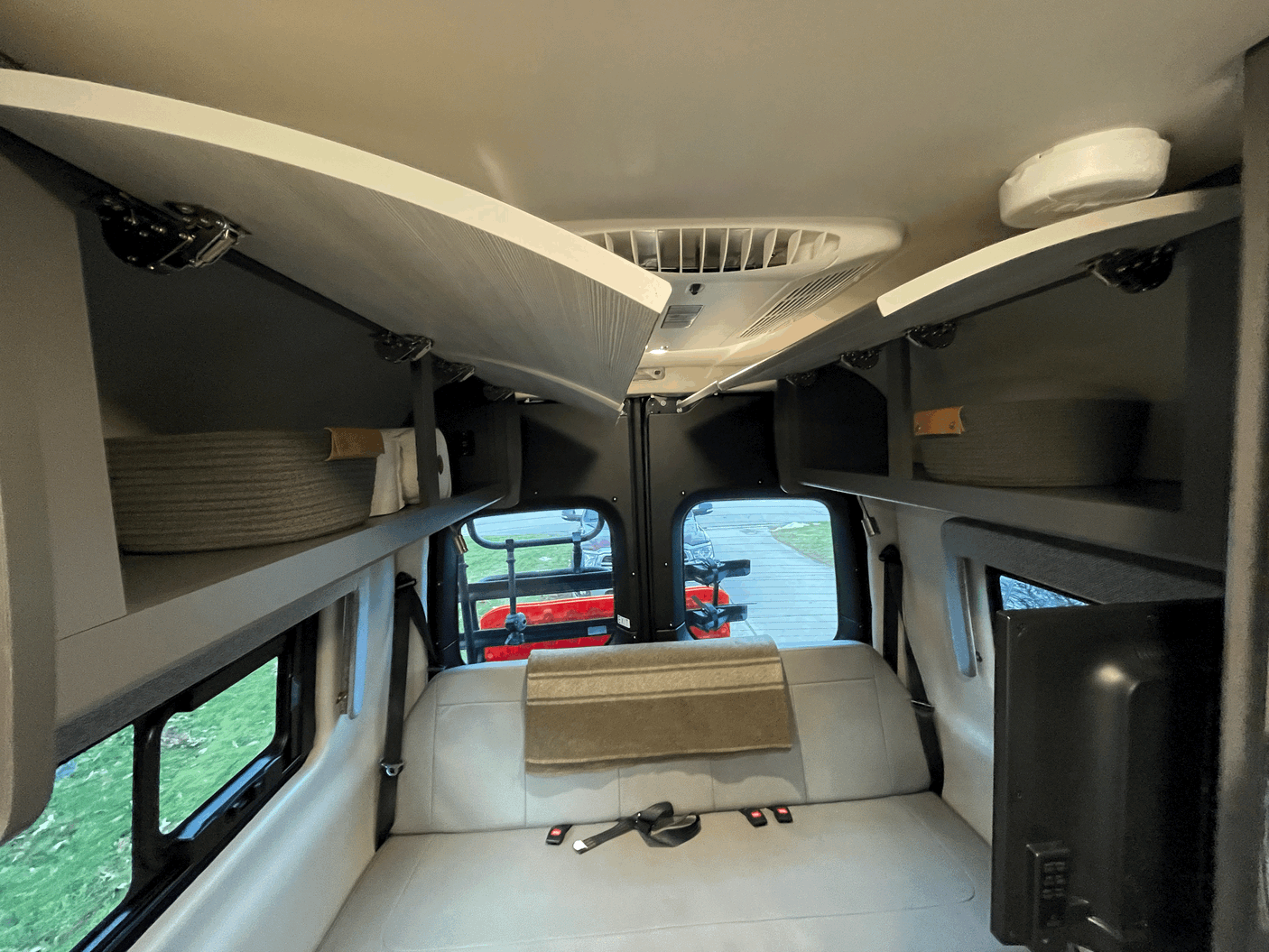 Inside an RV rental, featuring a rear bench seat/bed, open overhead cabinets, a ceiling AC unit, and rear windows.