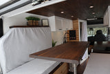 Experience a custom RV rental! This cozy interior features a warm wooden ceiling, white cabinets, and comfy grey seating with a dining table.