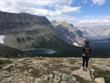 A hiker surveys majestic mountains and a serene lake. Explore these stunning views with an RV rental!