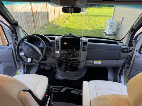 Spacious RV rental cockpit with Mercedes-Benz dashboard, modern controls, and comfortable light seats for an enjoyable journey.
